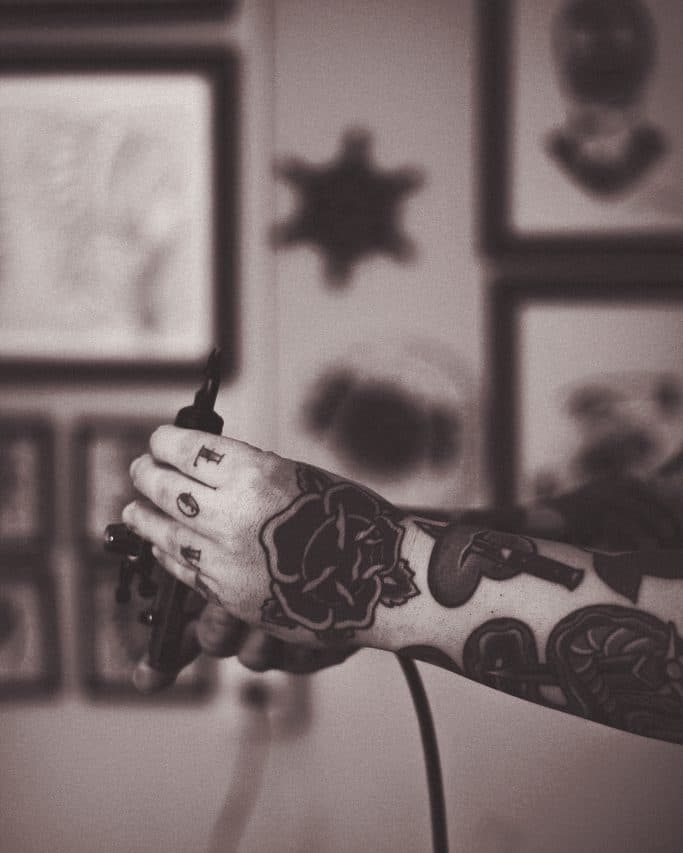 Tatoueur tenant sa machine, planches de flash au mur