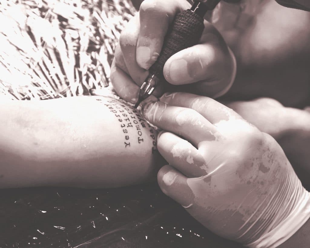 Mains gantées tatouant un poignet